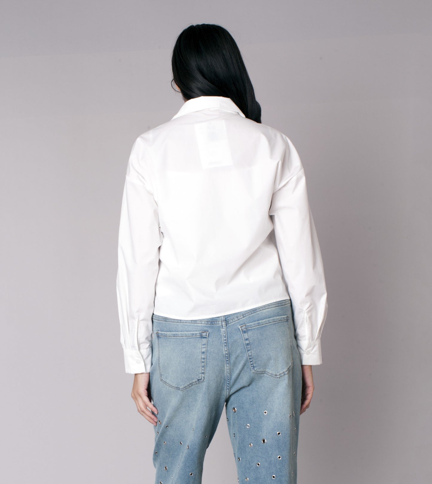 White cropped button-down shirt with denim star patch detailing on the front, model showing back view styled with denim jeans For Her NYC