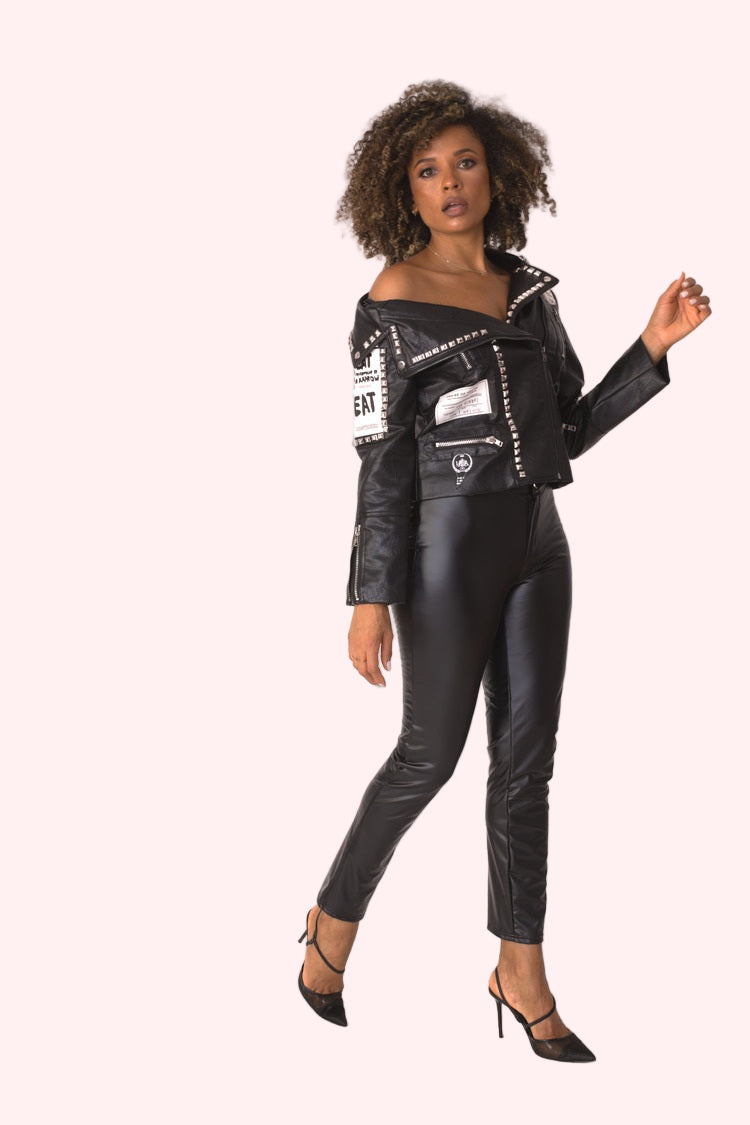 Model wearing black asymmetric faux leather jacket, front angled pose highlighting asymmetric neckline, textured faux leather finish, and edgy urban aesthetic by For Her NYC