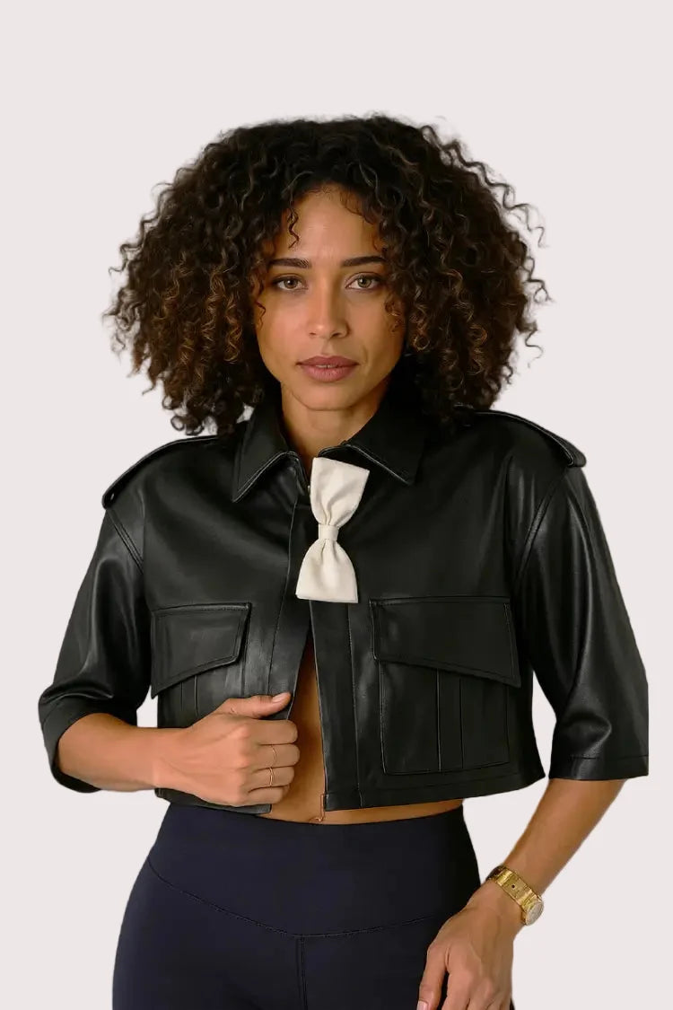 Front angle: Black cropped leather jacket with white bow accent, angled front pose, For Her NYC.