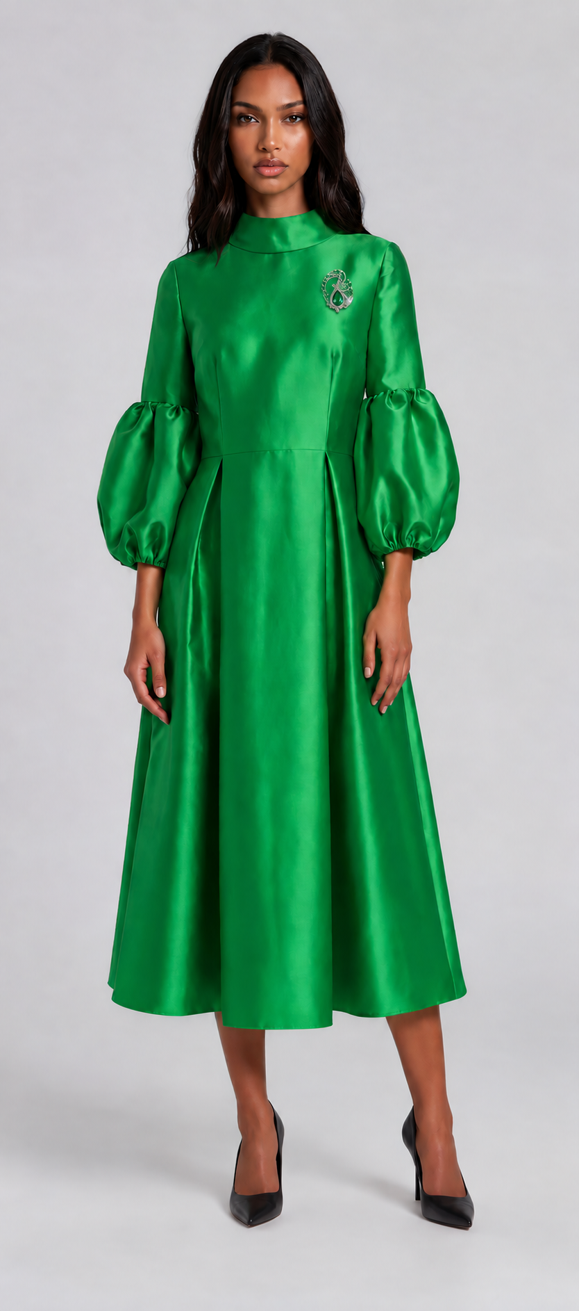 Woman wearing an emerald green satin midi dress featuring dramatic puff sleeves, a modest high neckline, and a flowing fit-and-flare silhouette. Tally Taylor.