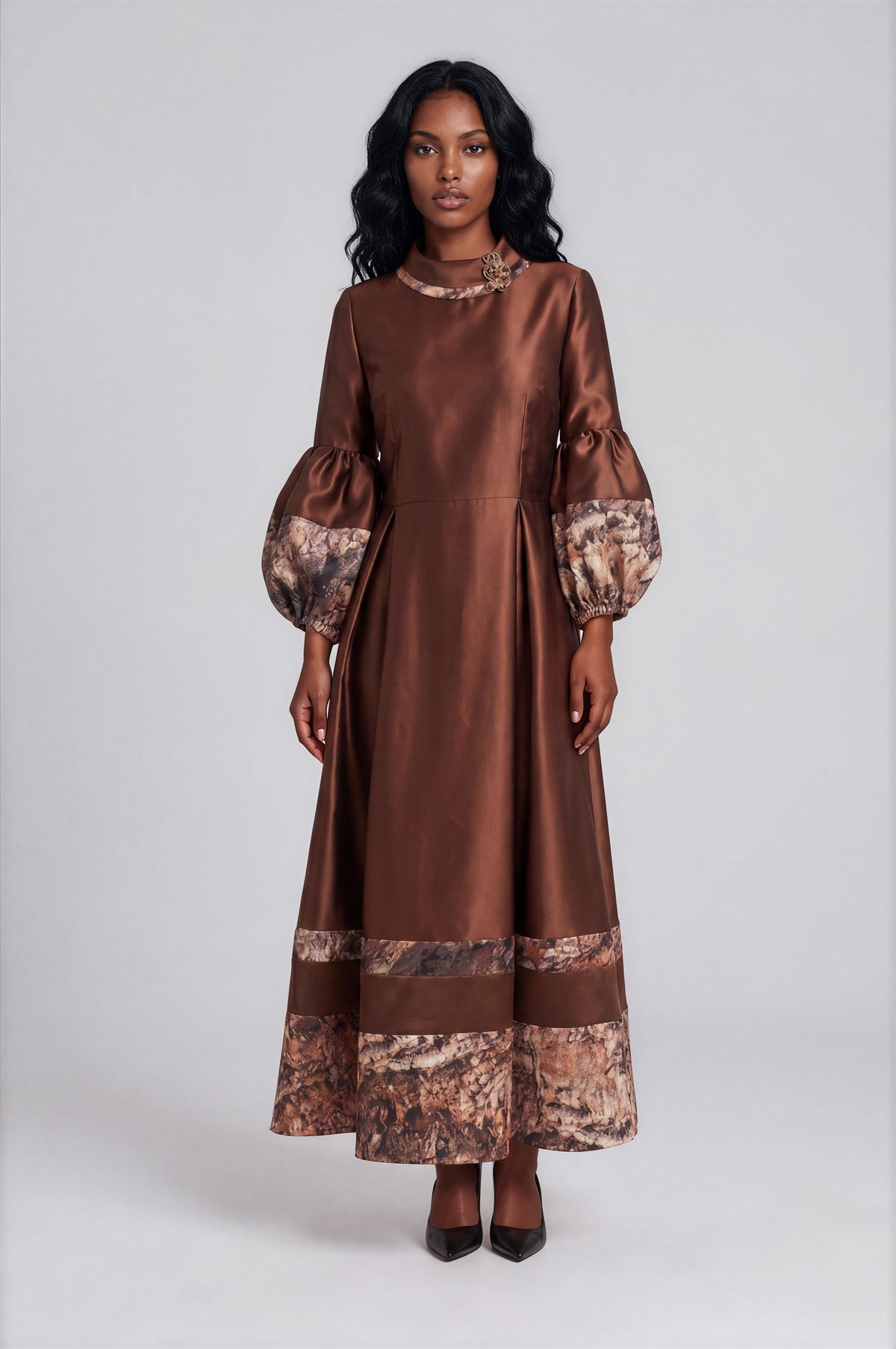 Front view of a model wearing the brown Tally Taylor Satin Maxi Dress with Printed Trim - 9879, featuring balloon sleeves, printed cuffs and hem, and a floral neckline embellishment