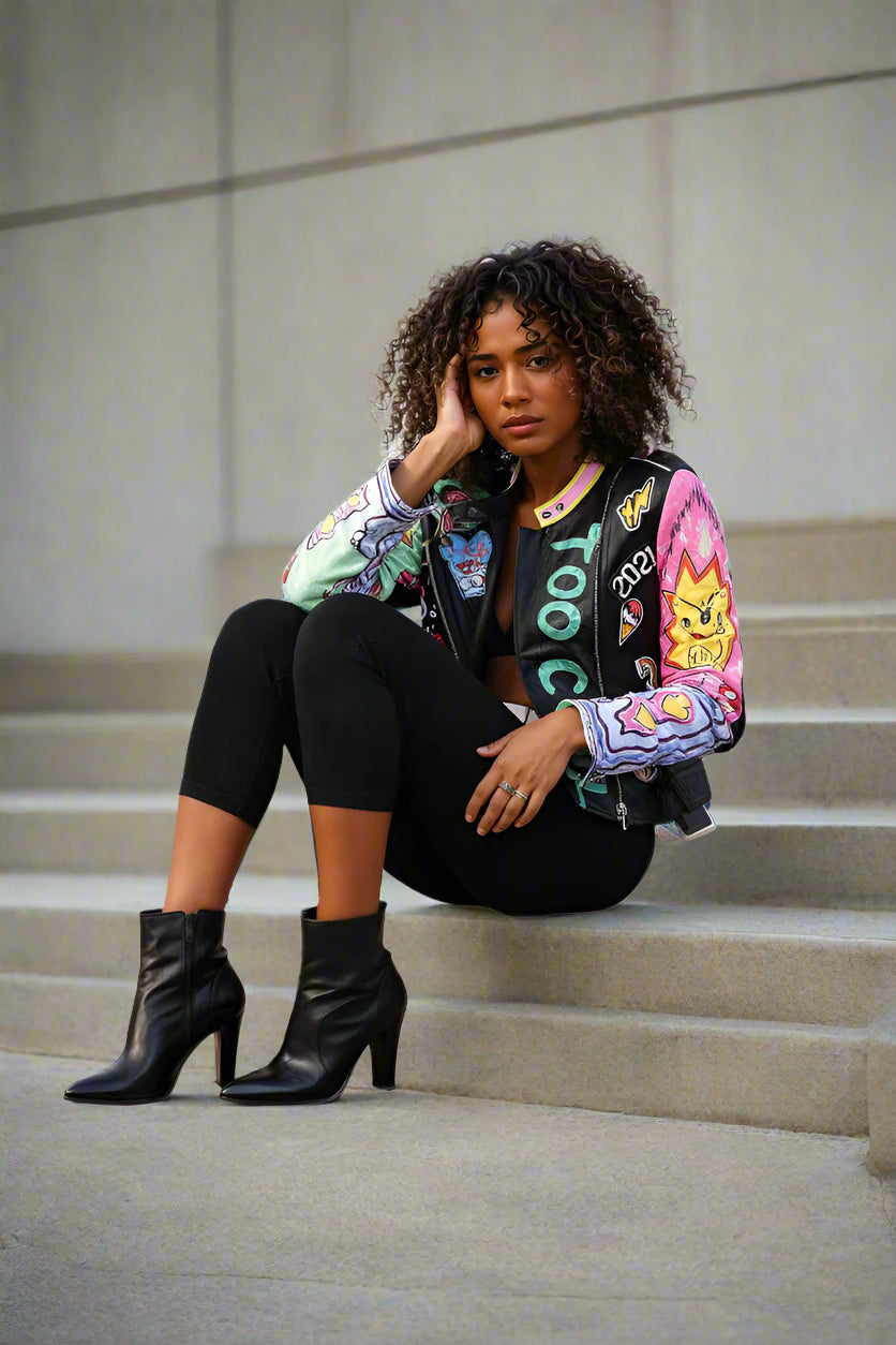 Seated stair pose showcasing the Vibrant Studded Leather Jacket black multi with bold graffiti details — For Her NYC