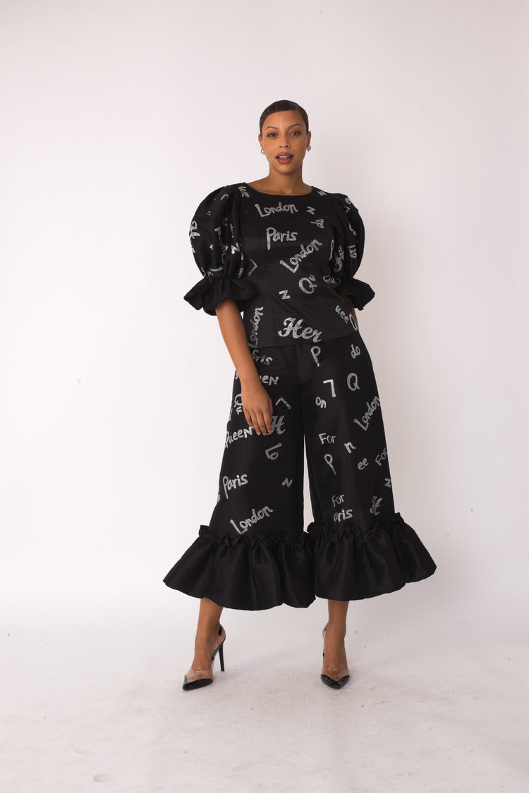 City Lights ruffle set style 82383 in black and silver shown in a walking forward pose emphasizing movement, layered ruffles, and the city-inspired metallic print by For Her NYC