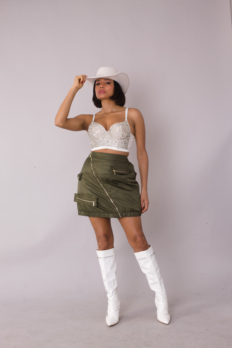 Model wearing utility cargo mini skirt in olive with diagonal zipper and pockets, front standing pose, For Her NYC