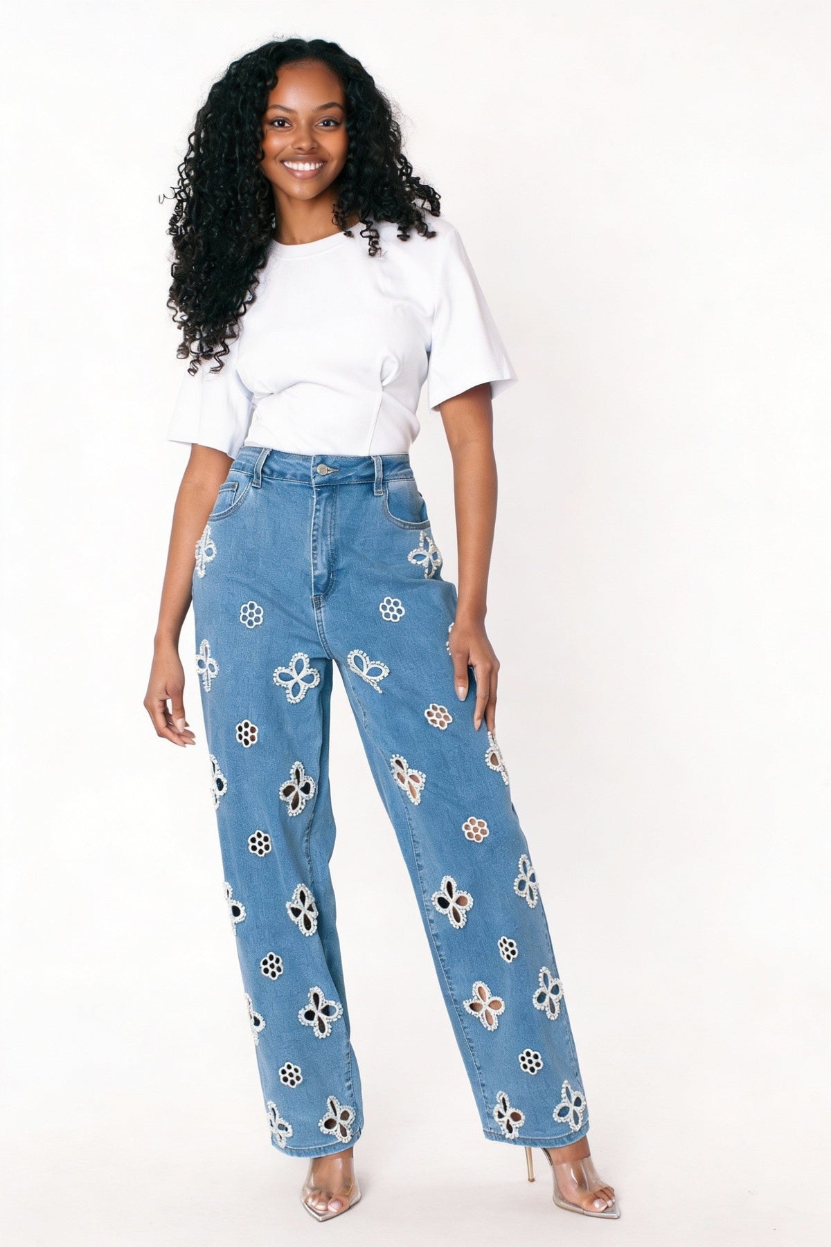 Denim wide-leg jeans with intricate floral cutout embellishments, model standing facing forward with one hand on hip wearing white top For Her NYC