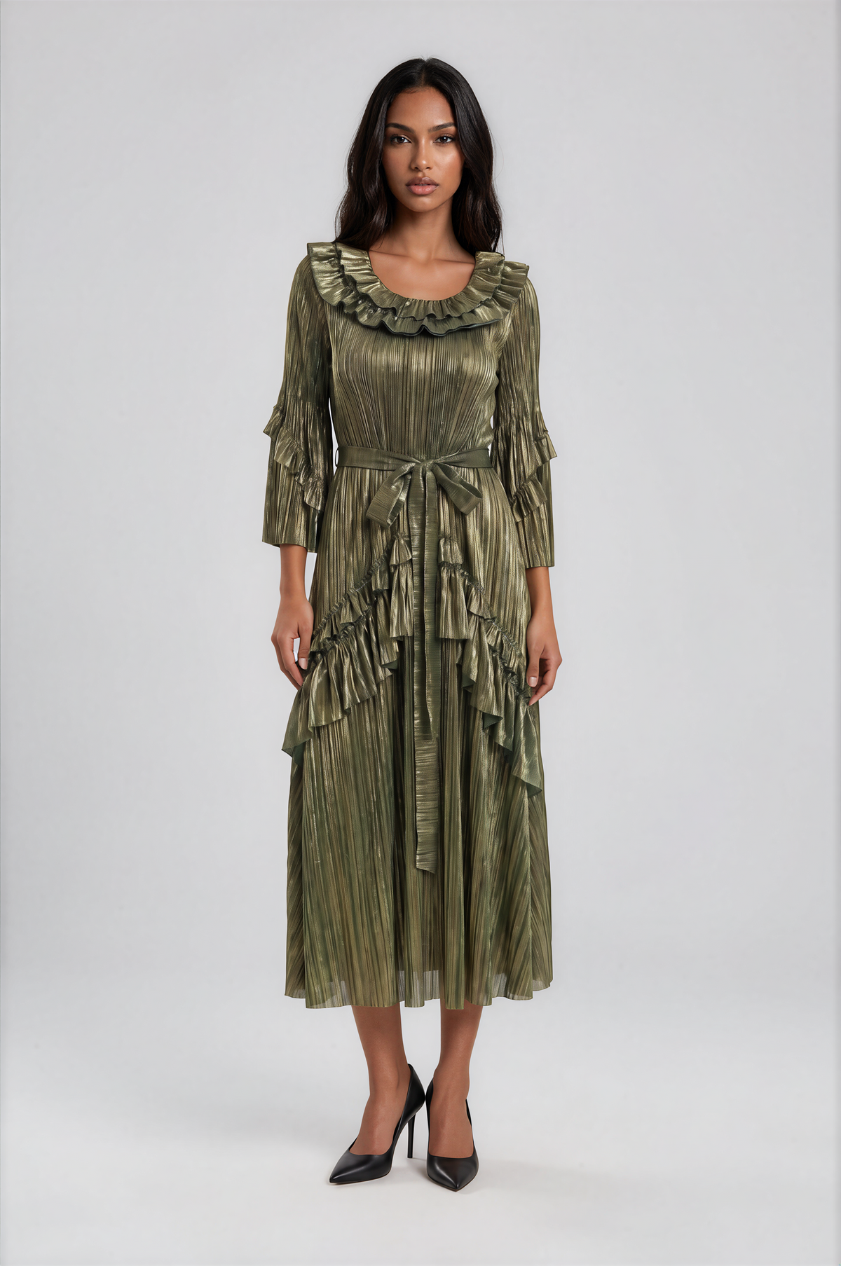 Woman modeling a green metallic pleated midi dress with cascading ruffle details, textured shimmer fabric, and flowing asymmetrical silhouette in a full front pose. For Her NYC