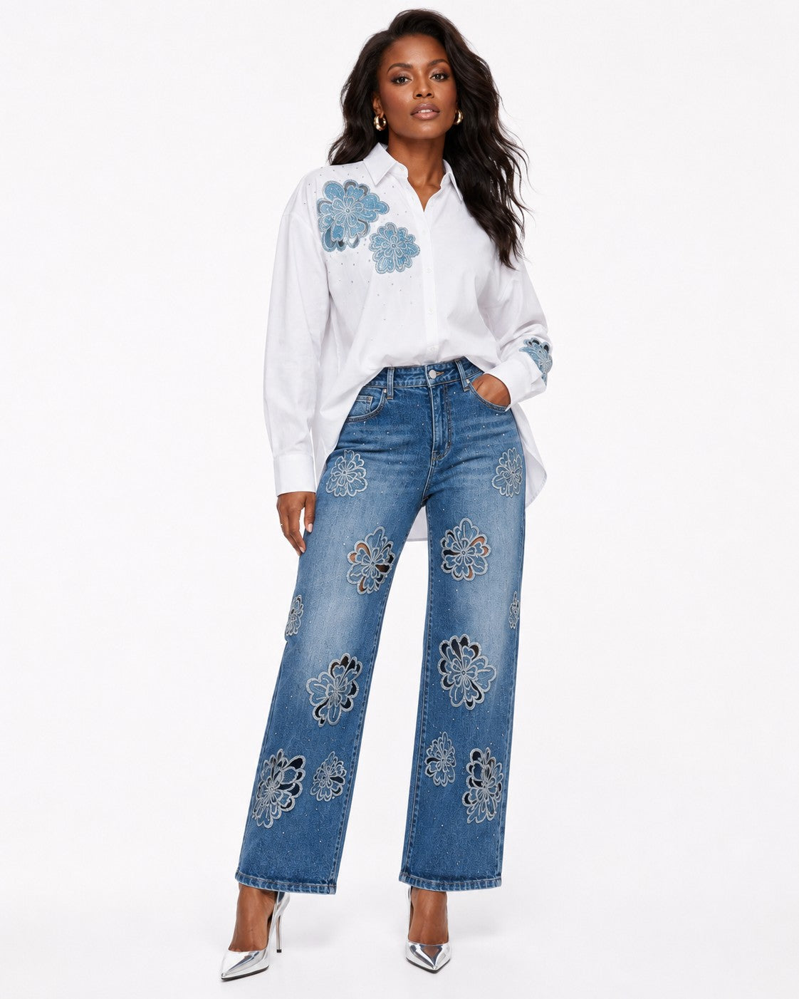 Model wearing a white button-down shirt with blue floral embroidery, paired with blue embellished jeans by For Her NYC