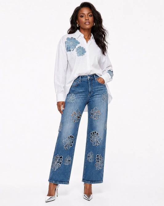Model wearing a white button-down shirt with blue floral embroidery, paired with blue embellished jeans by For Her NYC