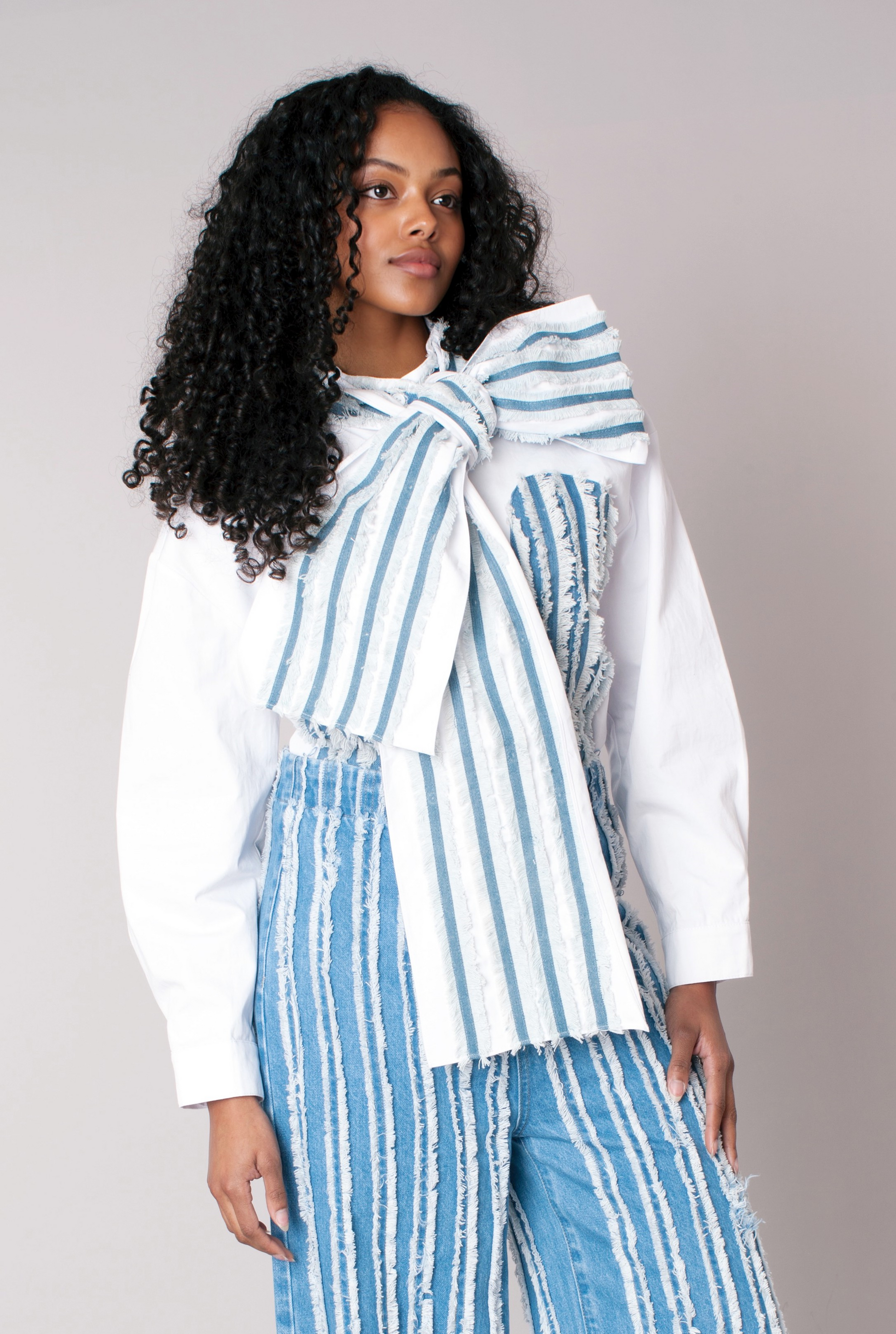 Angled view of asymmetric stripe wrap top highlighting oversized bow and stripe detail in white and denim For Her NYC