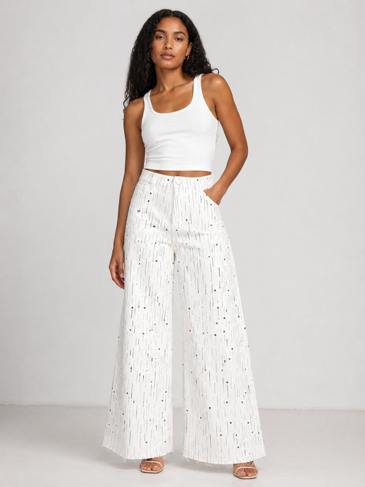 Model wearing the Crystal Stardust Embellished White Denim Jeans in white denim featuring sparkling crystal embellishments, a high-rise waist, and a wide-leg silhouette paired with a white tank top. For Her NYC.