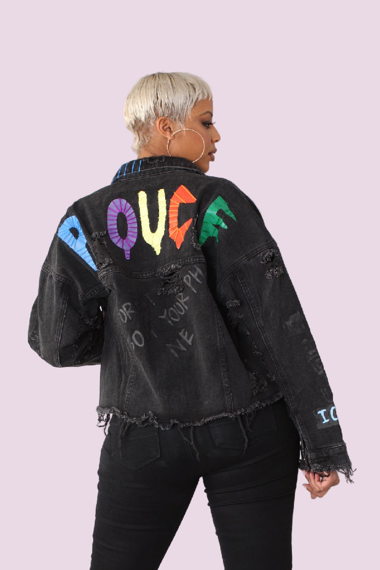 Black distressed denim jacket back view featuring bold colorful embroidered lettering and ripped detailing.
