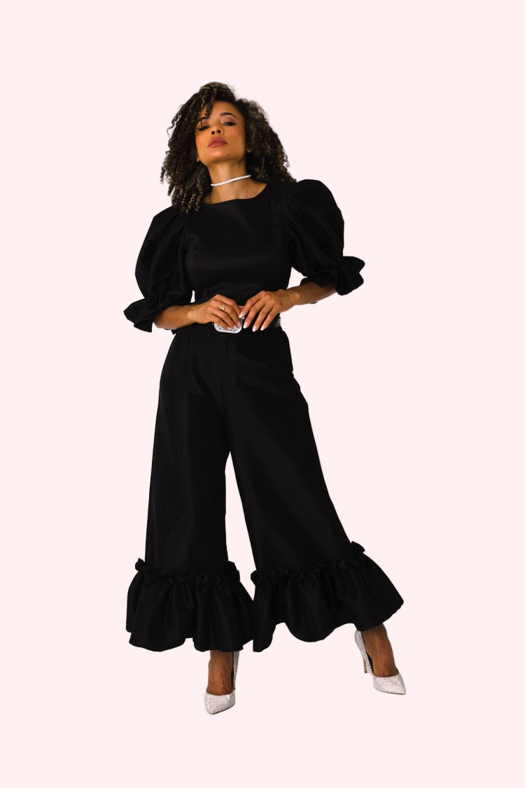 Model walking forward in black dramatic ruffle hem wide leg pants showcasing fluid movement by For Her NYC