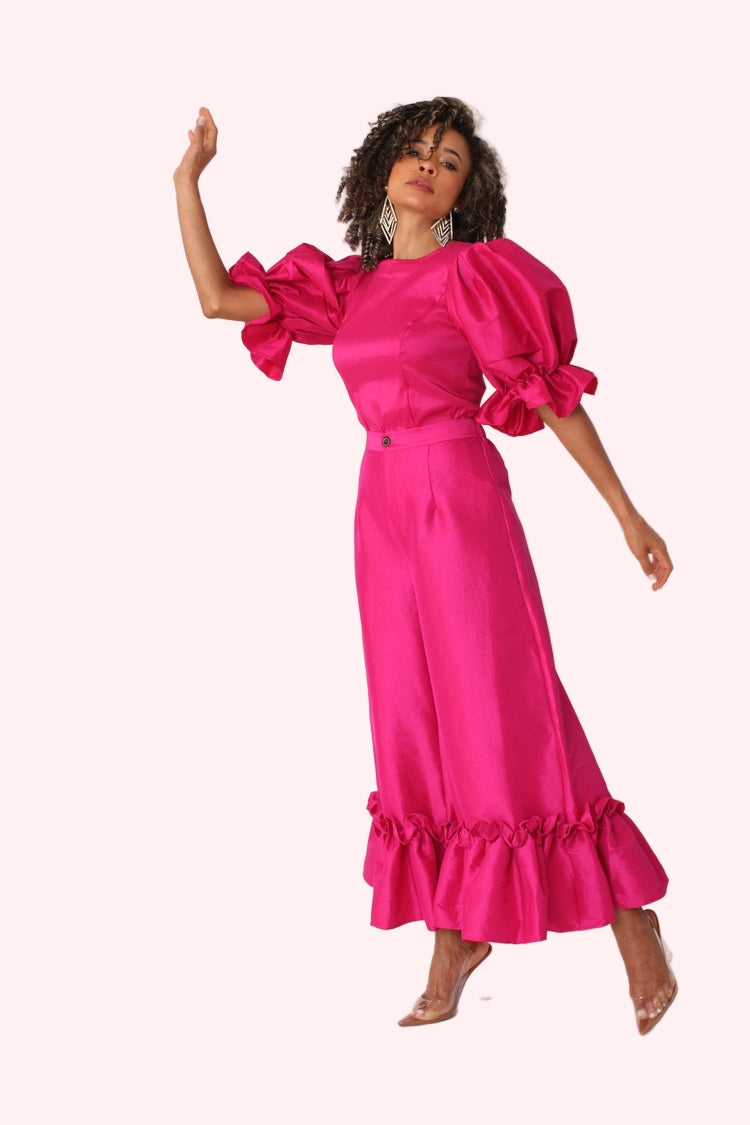 Model posing with raised arm in fuchsia dramatic ruffle hem wide leg pants showing playful movement by For Her NYC