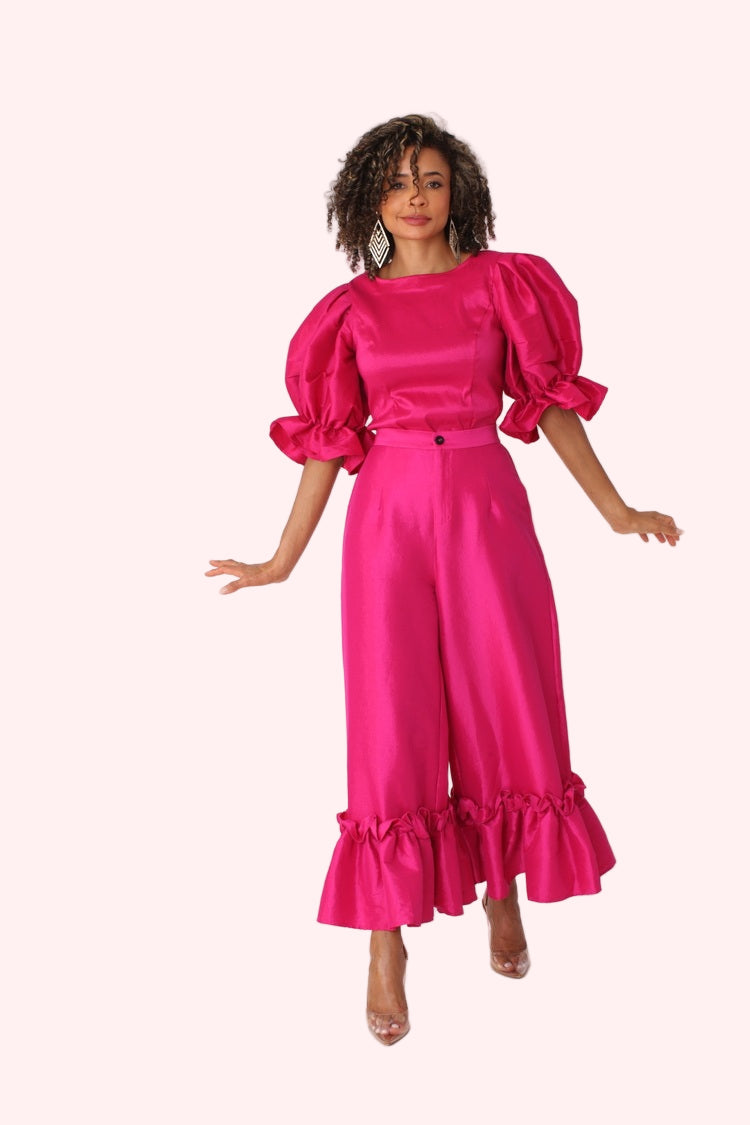 Model walking forward in fuchsia dramatic ruffle hem wide leg pants emphasizing flow and ruffle hem by For Her NYC