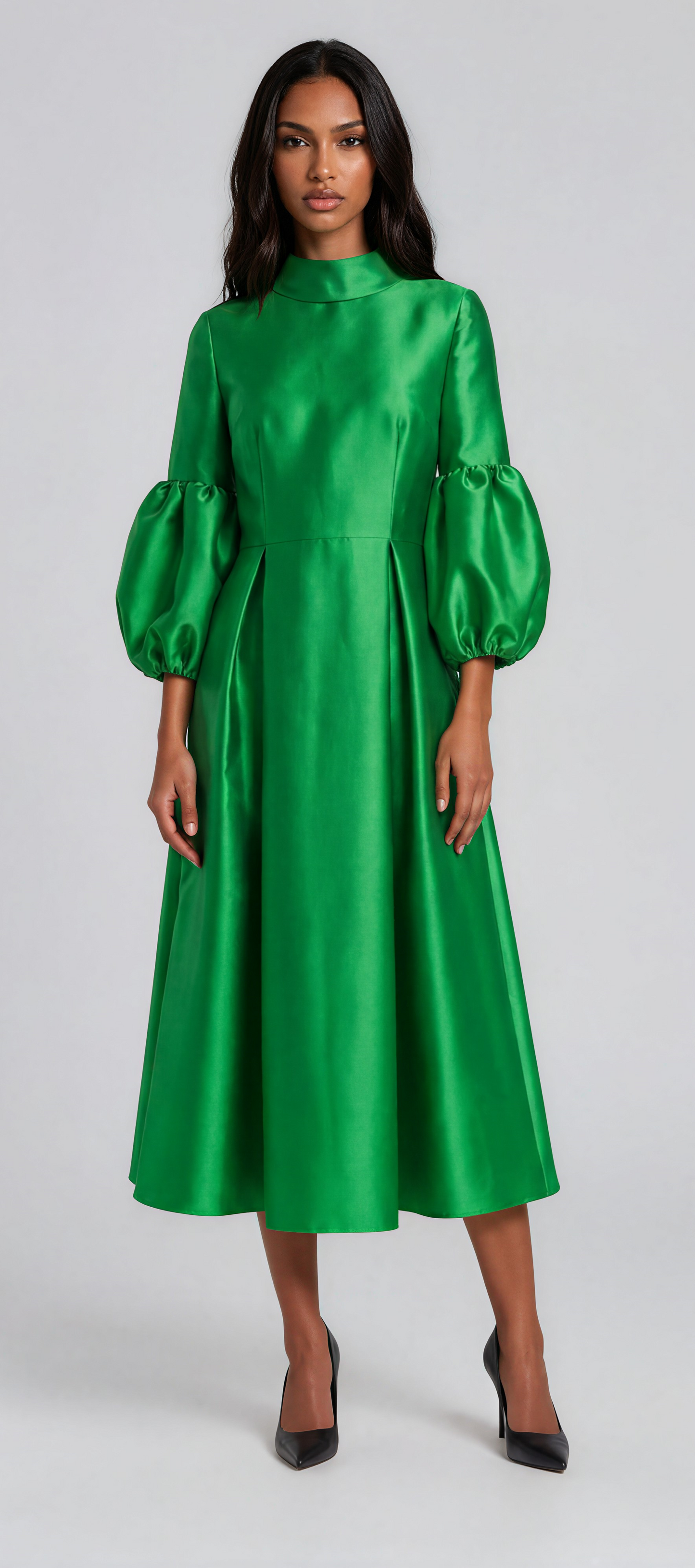 Woman wearing an emerald green satin midi dress featuring dramatic puff sleeves, a modest high neckline, and a flowing fit-and-flare silhouette. Tally Taylor.
