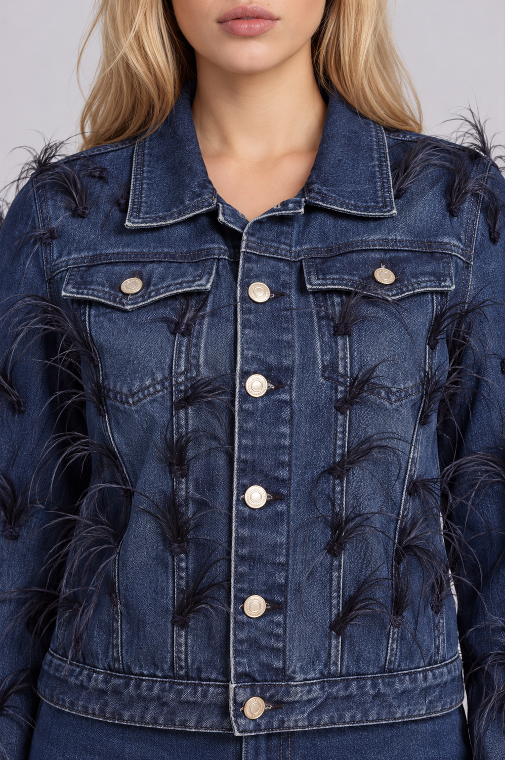Front close-up of a model wearing the dark-wash For Her NYC Feather Trim Denim Jacket - 82303 with feather embellishments, chest pockets, and metal buttons