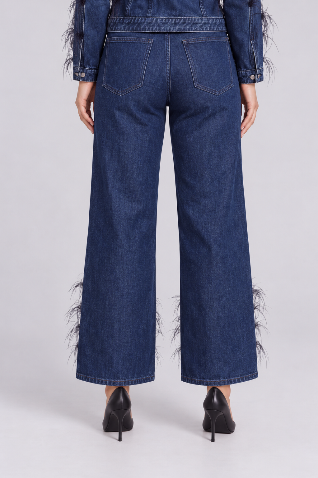 Back detail view of a model wearing the dark-wash For Her NYC Feather Trim Wide Leg Jeans - 82304 with back pockets and feather embellishments near the hems