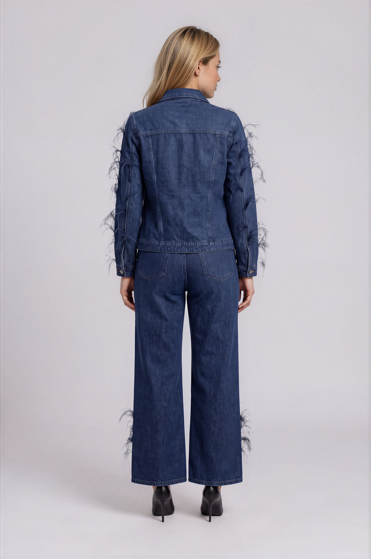Back view of a model wearing the dark-wash For Her NYC Feather Trim Wide Leg Jeans - 82304 with back pockets, wide legs, and feather embellishments near the hems