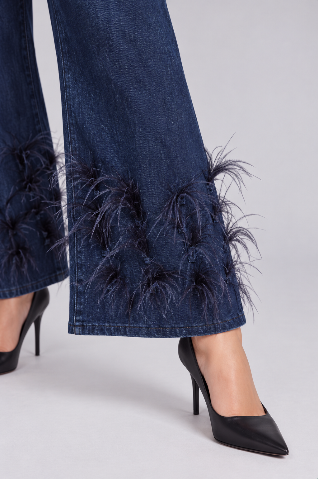 Extended-leg close-up of a model wearing the dark-wash For Her NYC Feather Trim Wide Leg Jeans - 82304, highlighting the feather embellishments near the hem