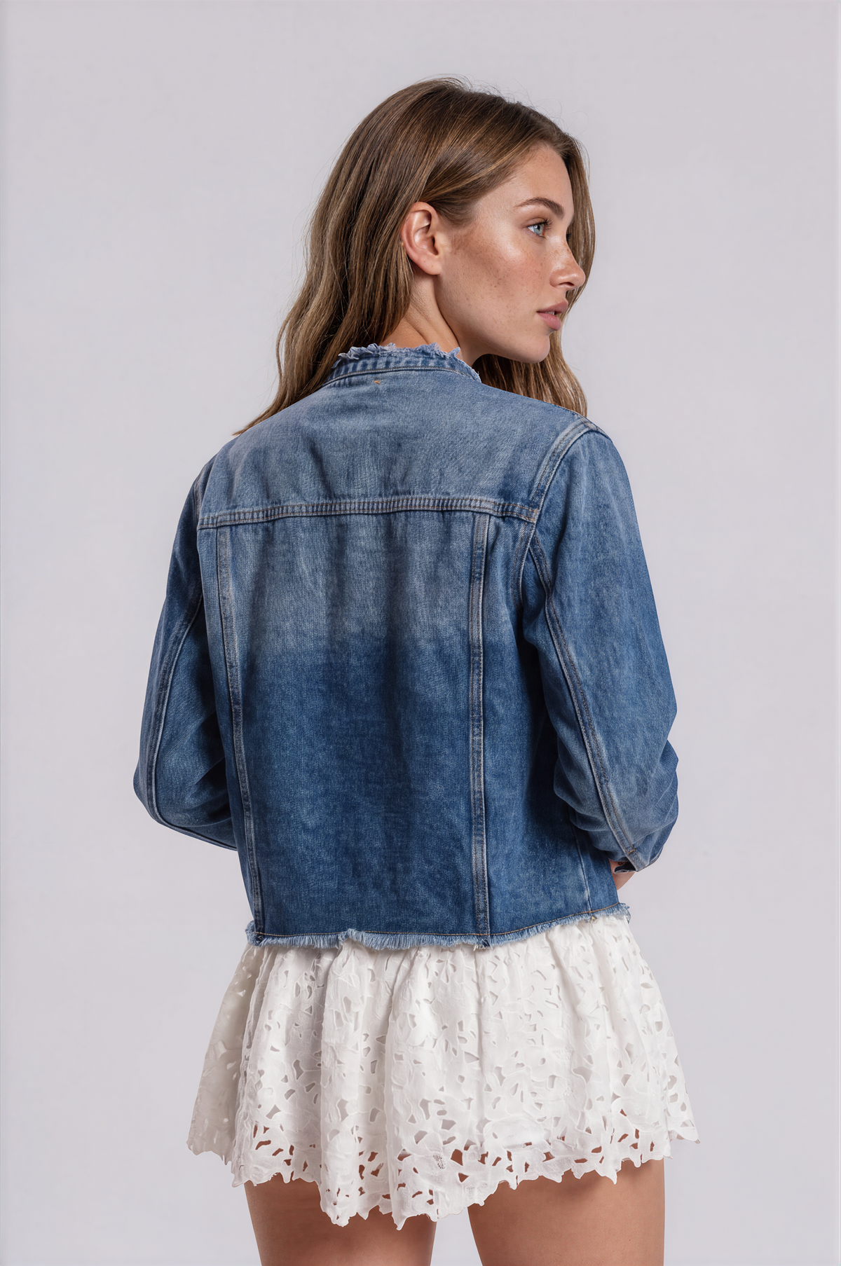 Back view of a model wearing the For Her NYC Pearl Button Denim Jacket - 83040 with a washed finish and frayed hem