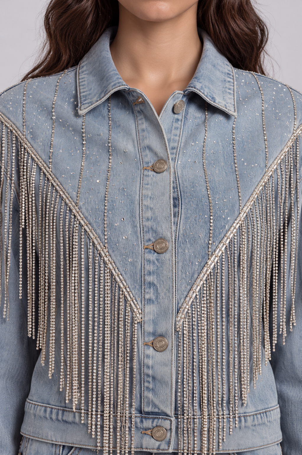 Front close-up of a model wearing the light-wash For Her NYC Rhinestone Fringe Denim Jacket - 82938 with a button front and cascading rhinestone fringe