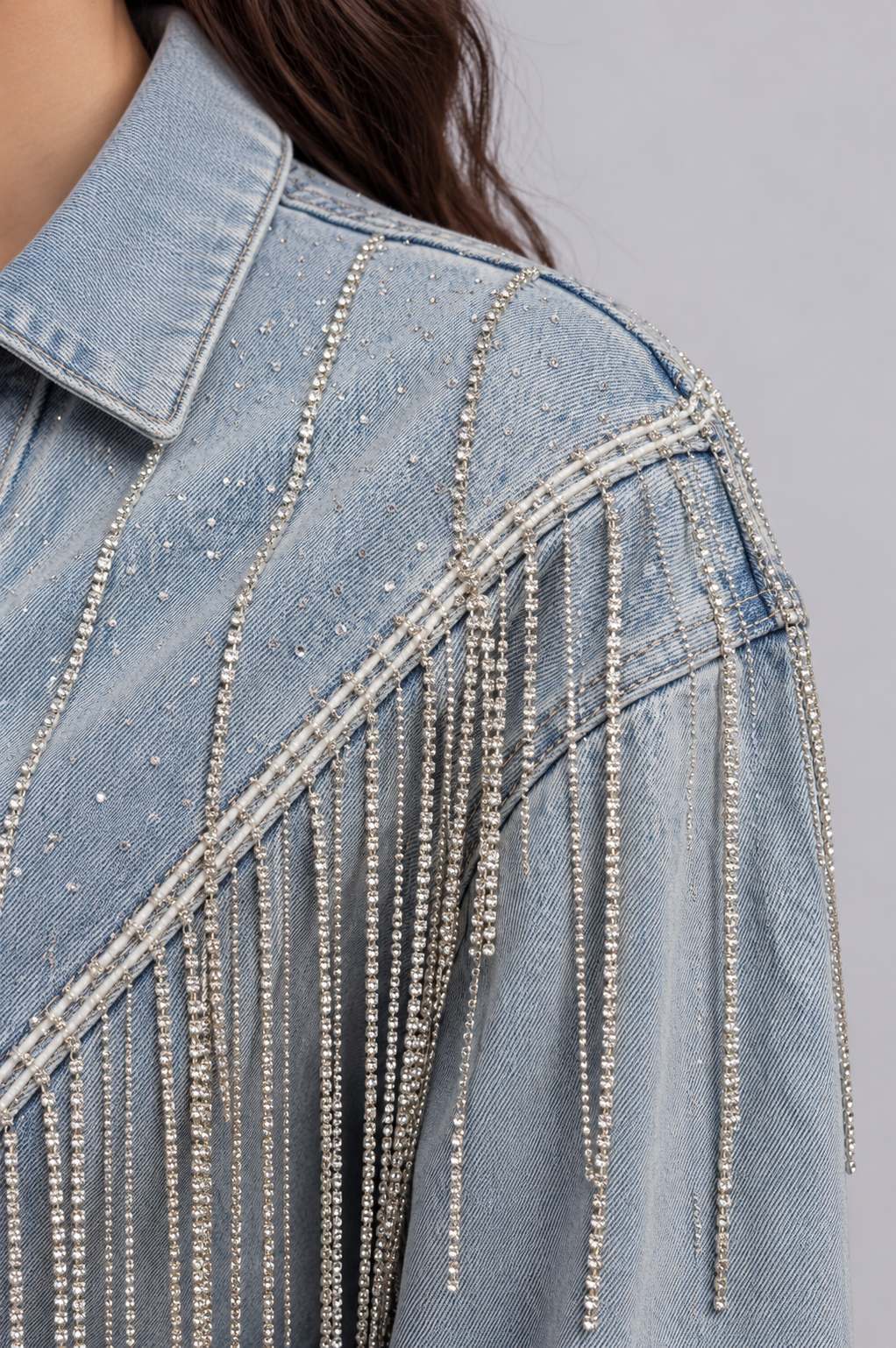 Shoulder close-up of a model wearing the light-wash For Her NYC Rhinestone Fringe Denim Jacket - 82938, highlighting the rhinestone embellishments and cascading fringe