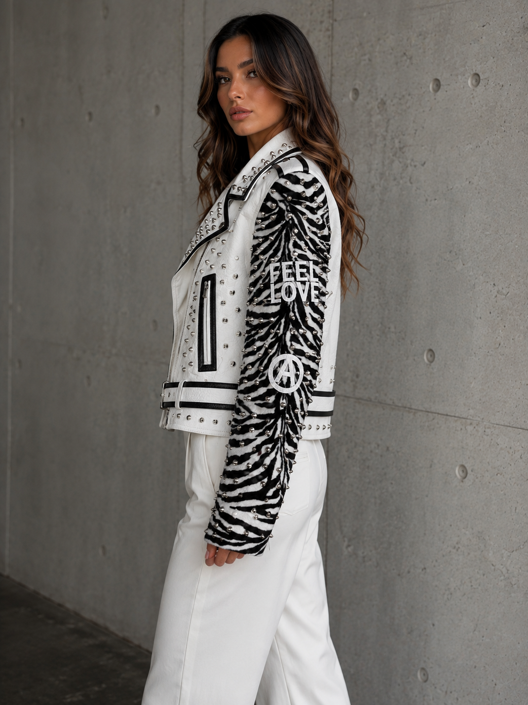 Faux leather jacket with detachable sleeves styled with white pants, front pose.