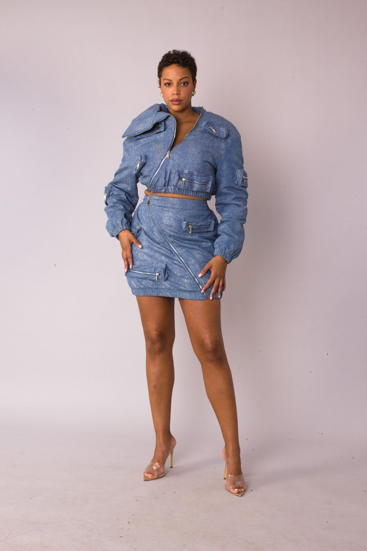 Model wearing the denim silver metallic shimmer mini skirt standing front facing, featuring asymmetrical zip detail and functional pockets by For Her NYC