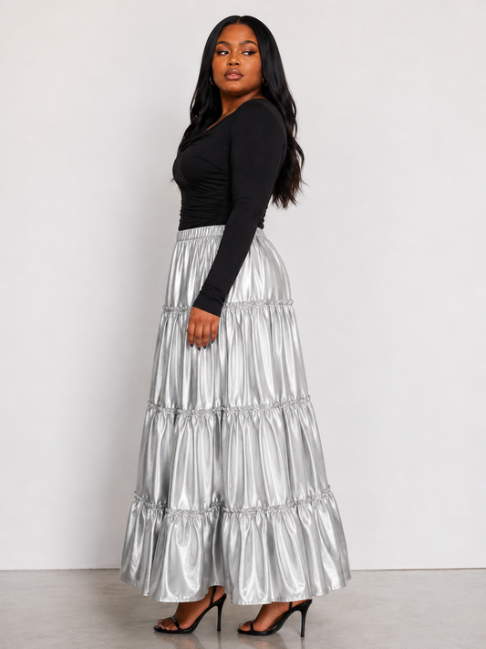 Model wearing the silver metallic tiered maxi skirt standing facing the side, showcasing lustrous finish and dramatic tiered silhouette by For Her NYC
