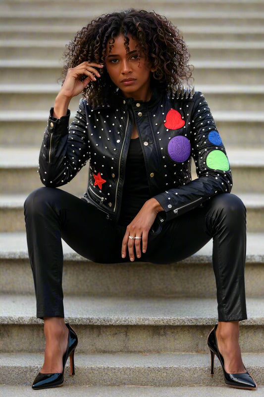 Black multi-colored studded leather moto jacket, seated on steps — For Her NYC