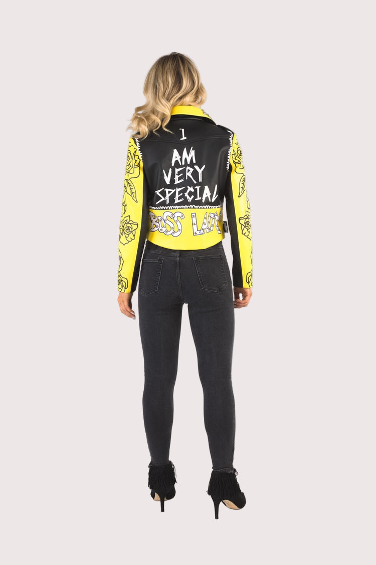 Model wearing YELLOW/BLACK faux leather jacket with pins and studs, full back view highlighting statement text detail and yellow printed sleeves by For Her NYC