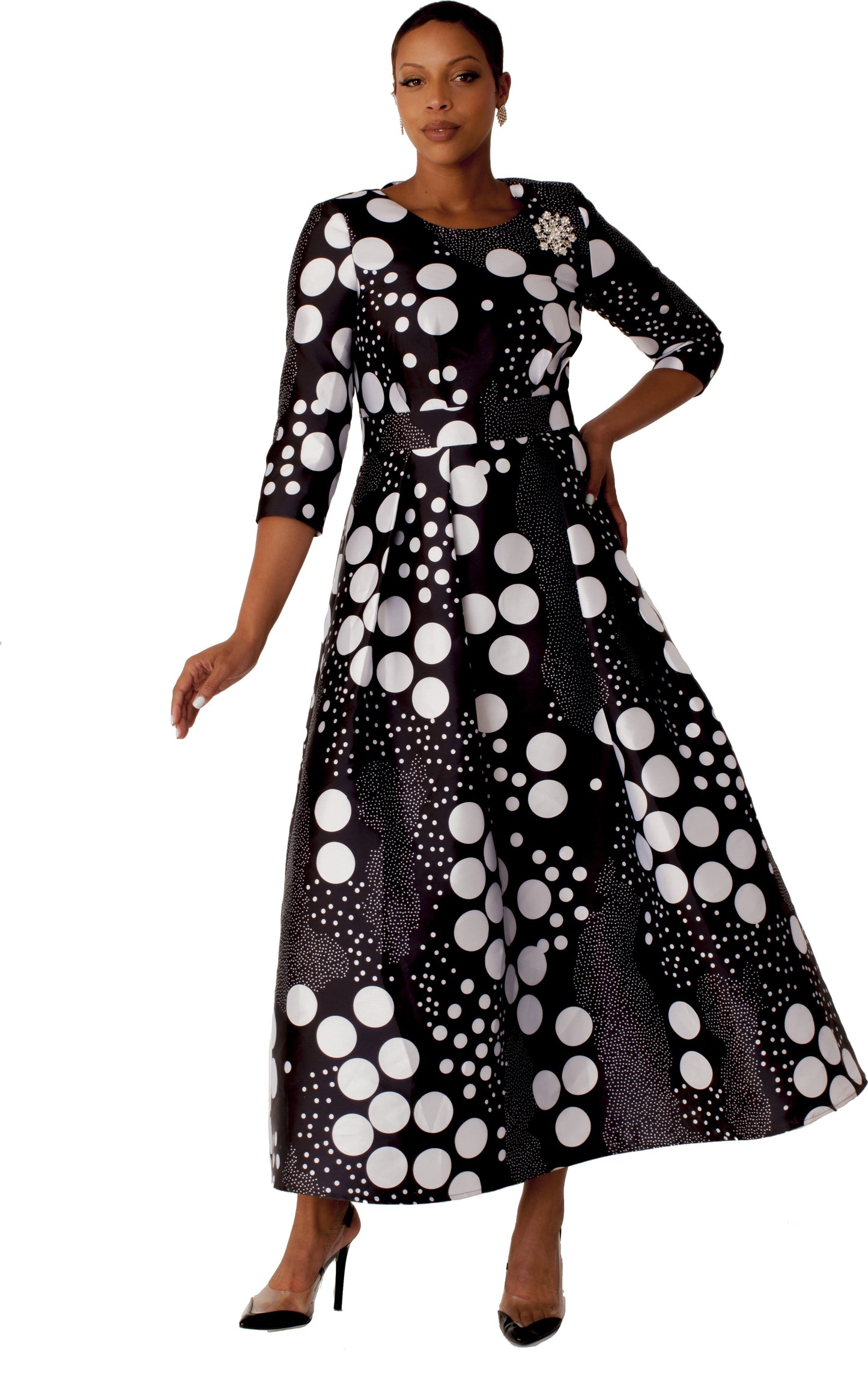 Model wearing black and white dot print plus size satin dress with rhinestone brooch, front standing pose by Tally Taylor