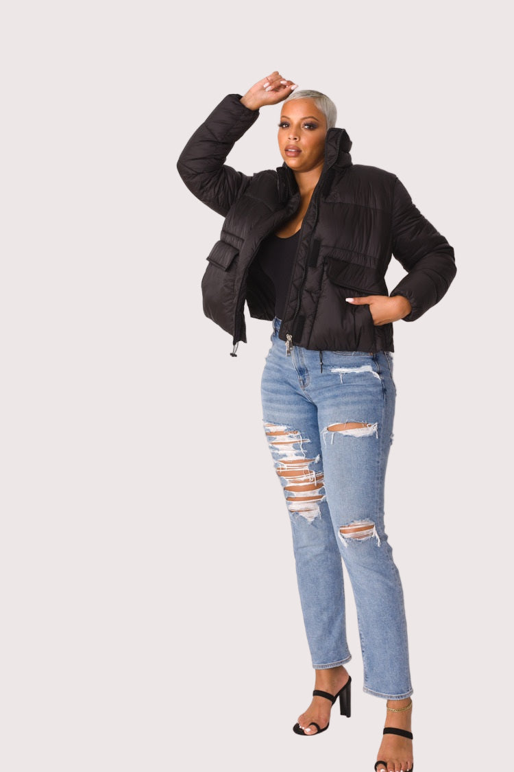Model wearing black plush puffer jacket, front pose with hands near collar showcasing cozy faux fur exterior and cold-weather styling by For Her NYC