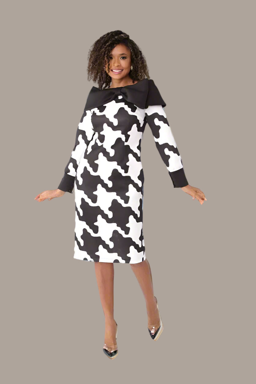 Model wearing a black and white printed scuba dress with long sleeves and an oversized bow collar, standing front-facing in a studio — For Her NYC