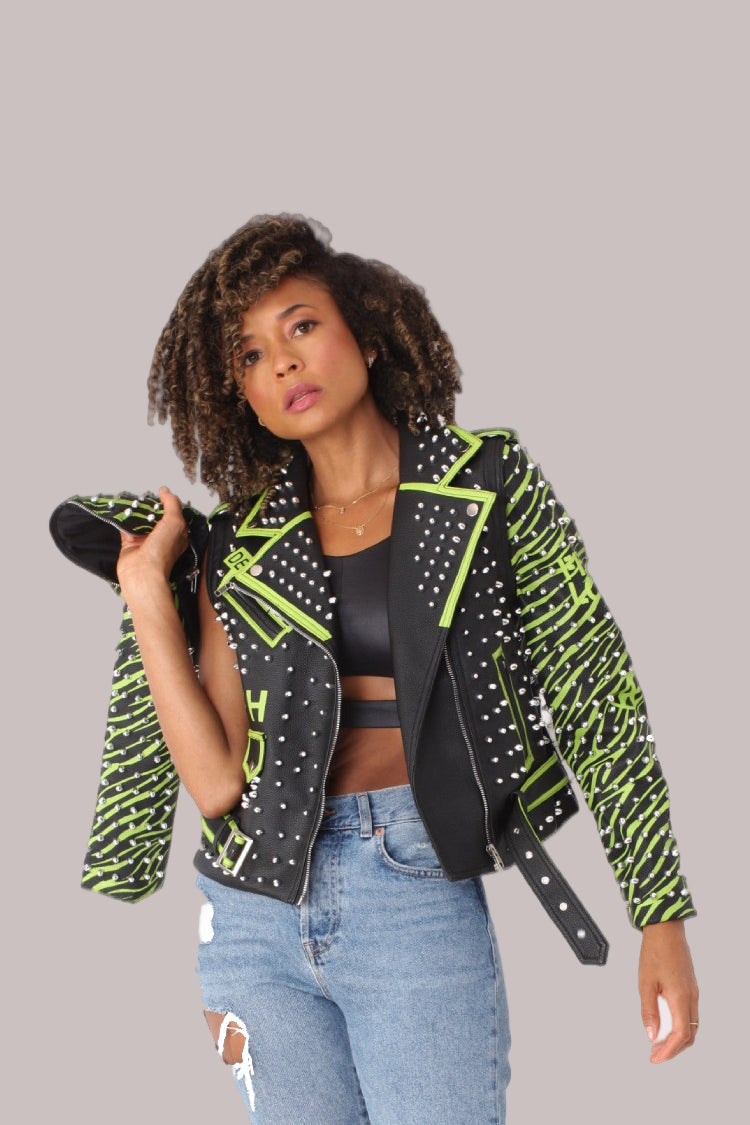 Model wearing a black and lime studded leather jacket with detachable sleeves in a front standing pose, showcasing silver studs and vibrant lime accents, For Her NYC