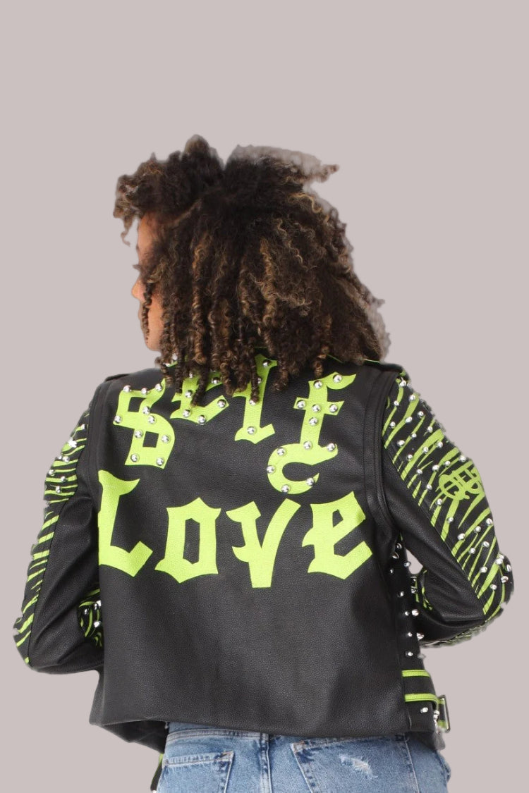 Model wearing a black and lime studded leather jacket with detachable sleeves in a front walking pose, highlighting movement and bold graphic styling, For Her NYC