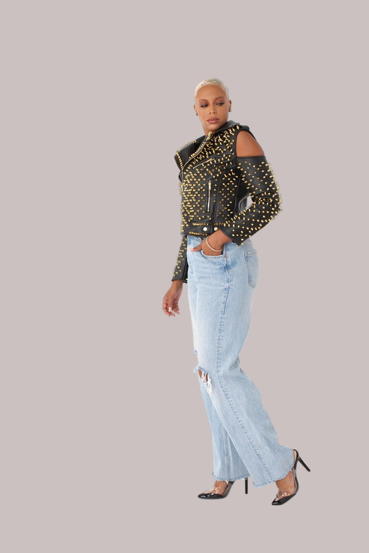 Black/Gold studded pleather moto jacket with open shoulders shown in side walking view, emphasizing silhouette and stud detailing by For Her NYC
