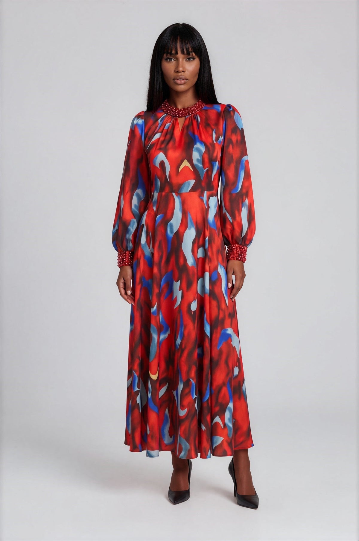 Front view of a model wearing the Tally Taylor Marbella Printed Maxi Dress - 41038 in red, blue, and black with an abstract print, long sleeves, and beaded neckline and cuffs