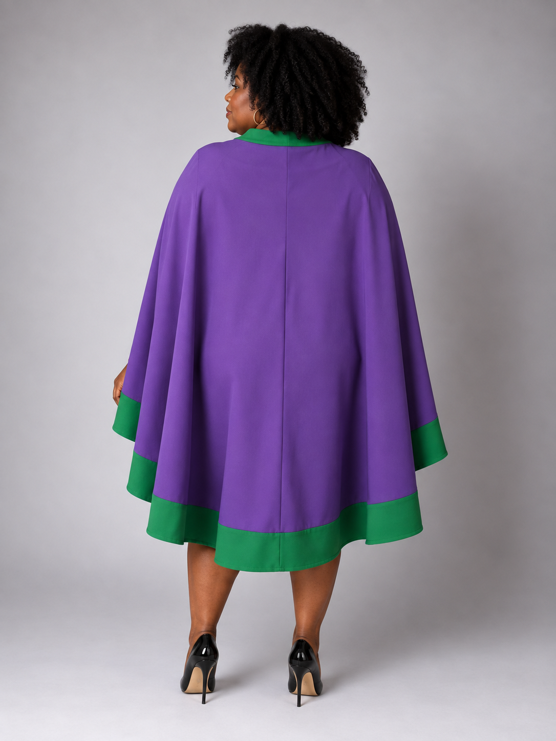 Back view of a plus-size model wearing the Tally Taylor Plus Size Cape Sheath Dress - U0617W in purple with green trim and a flowing cape
