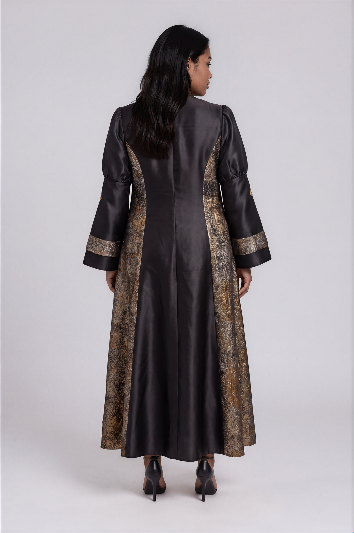 Back view of a plus-size model wearing the black and gold Tally Taylor Plus Size Contrast Panel Bell Sleeve Clergy Robe - 4565W with metallic side panels and bell sleeves