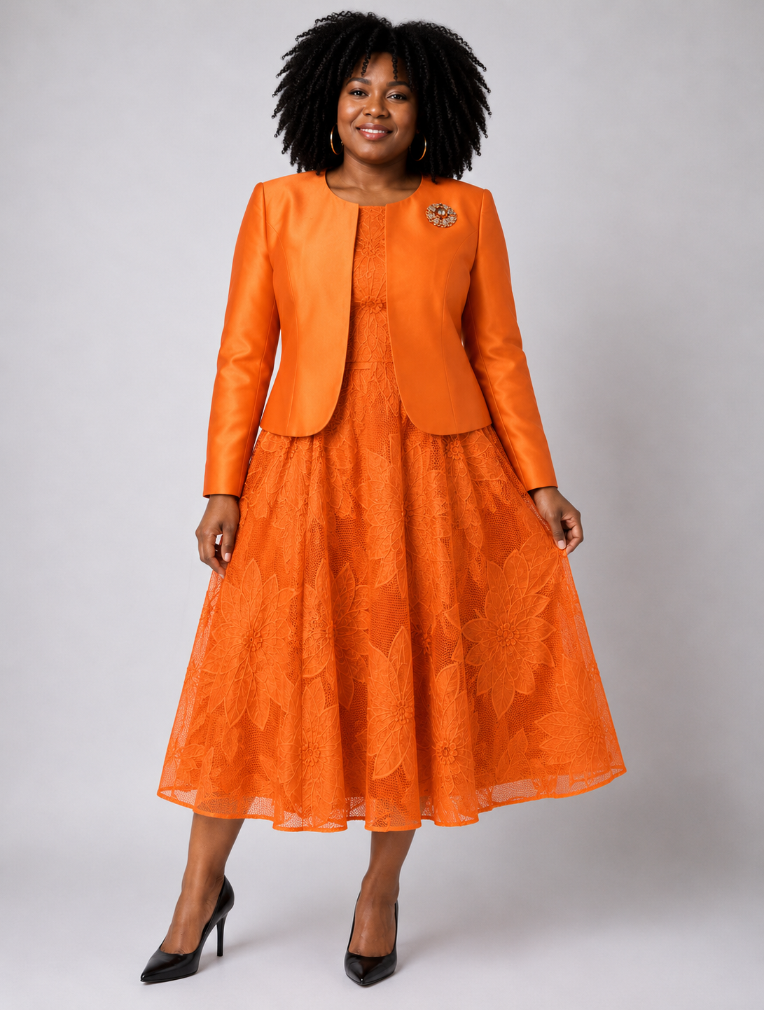 Plus size model wearing the Tally Taylor Floral Lace Dress & Satin Jacket Set in burnt orange, featuring a floral lace midi dress with a coordinating satin jacket and jeweled brooch.