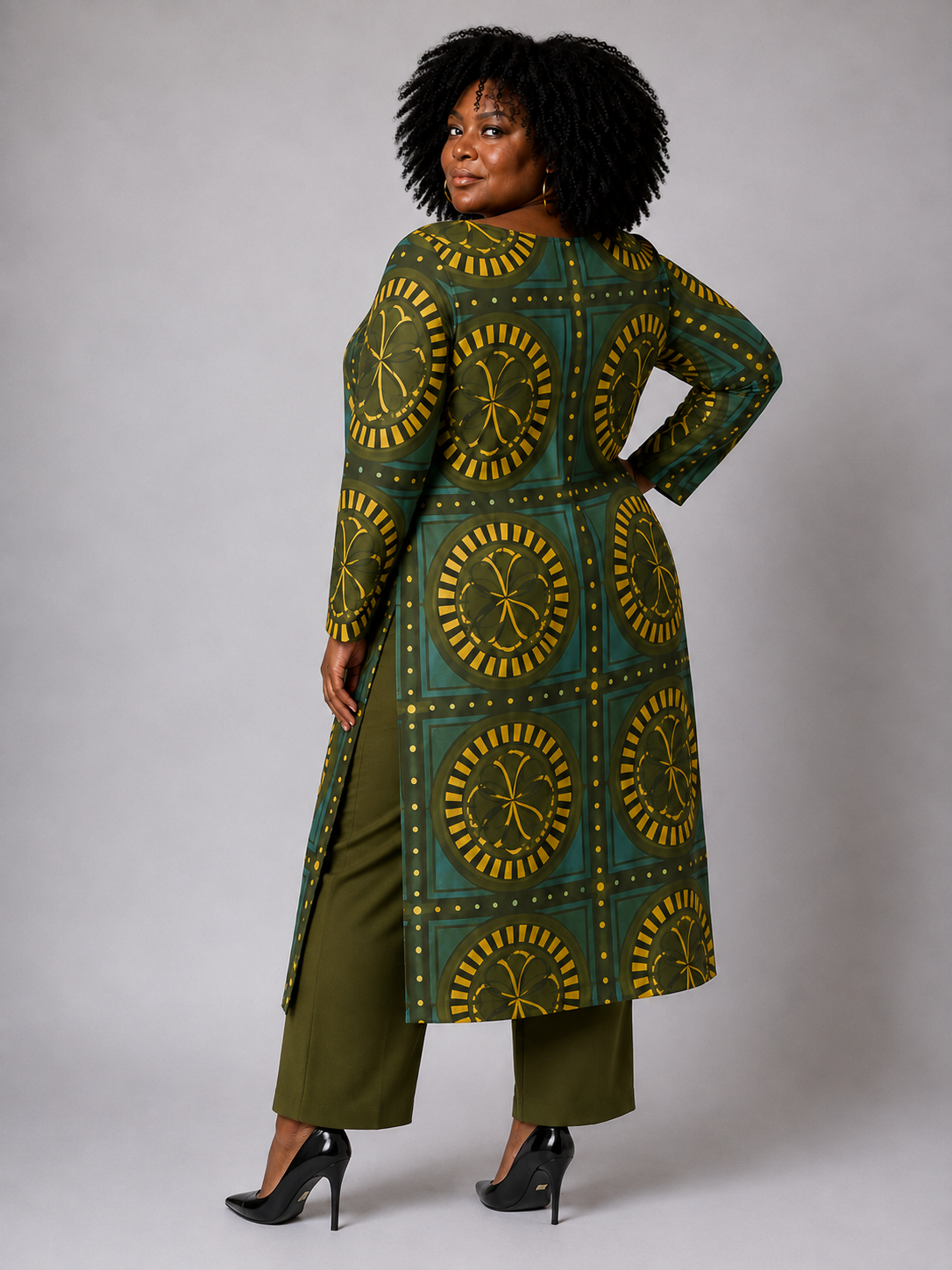 Plus size model showing the back of the Tally Taylor Geo Circle Print Long Tunic Pant Set in olive green, featuring a bold geometric print, side slits, and coordinating pants, style S0274W.