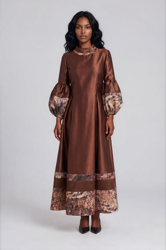 Front view of a model wearing the brown Tally Taylor Satin Maxi Dress with Printed Trim - 9879, featuring balloon sleeves, printed cuffs and hem, and a floral neckline embellishment