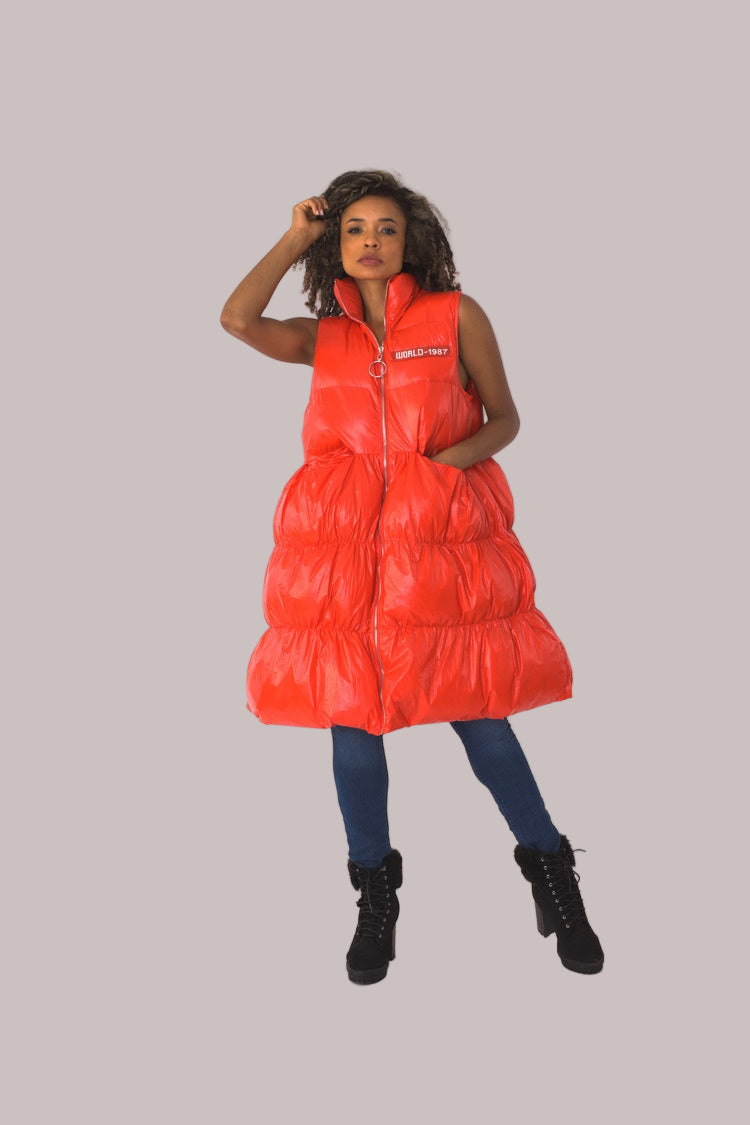 Front view of red tiered puffer vest with one hand raised and collar detail — For Her NYC.