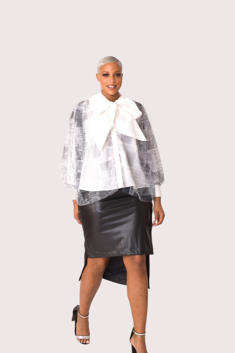 Model wearing newsprint tulle puff sleeve top with bow collar, angled front pose highlighting graphic contrast and fashion-forward detailing by For Her NYC