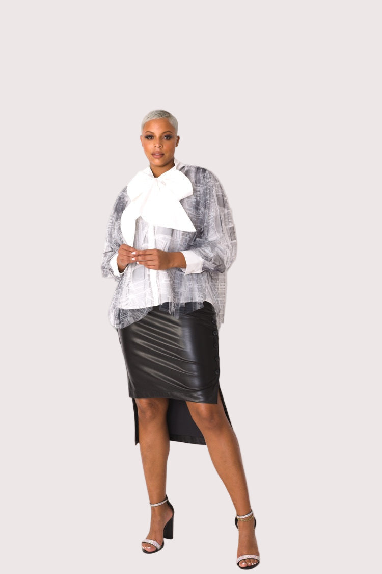Model wearing newsprint tulle puff sleeve top with bow collar, front-facing hero pose highlighting bold graphic print and dramatic puff sleeves by For Her NYC