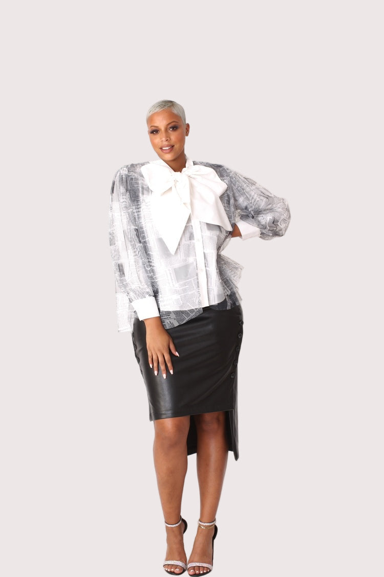 Model wearing newsprint tulle puff sleeve top with bow collar, front standing pose emphasizing statement print placement and structured silhouette by For Her NYC