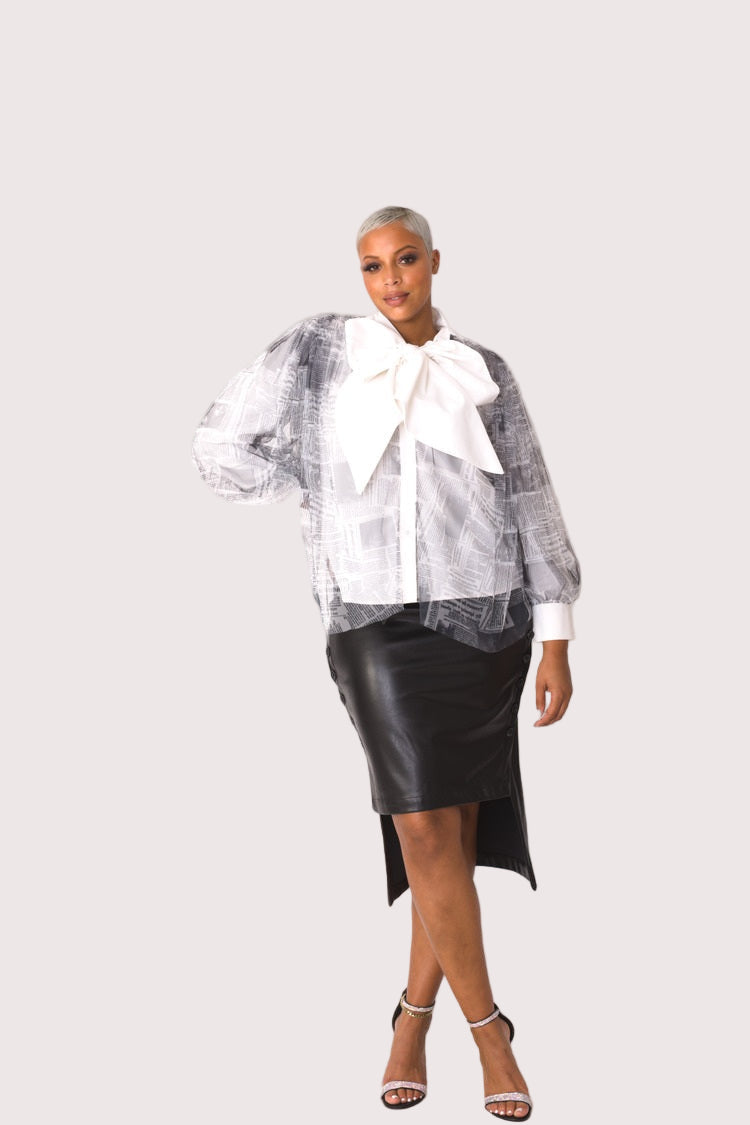 Model wearing newsprint tulle puff sleeve top with bow collar, front walking pose showing movement in tulle sleeves and editorial-style print by For Her NYC