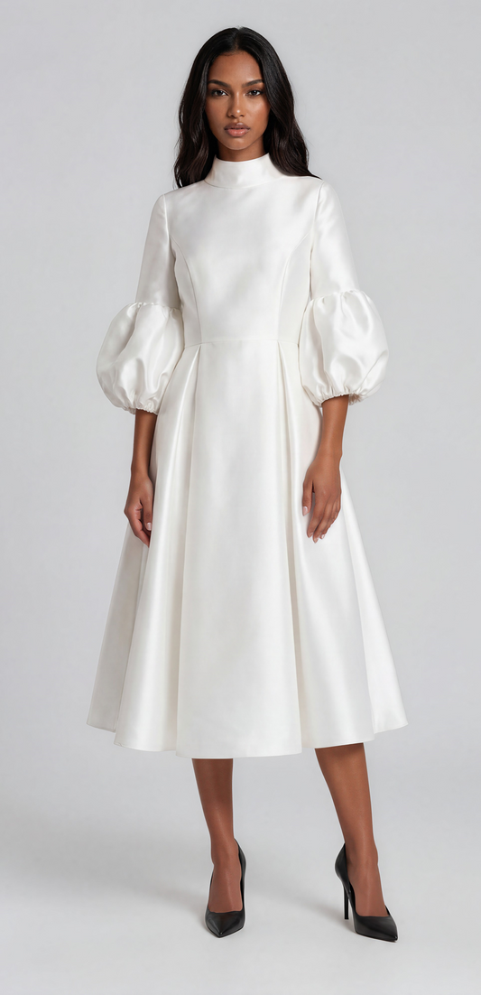 Woman wearing a white satin midi dress featuring dramatic puff sleeves, a modest high neckline, and a flowing fit-and-flare silhouette. Tally Taylor.